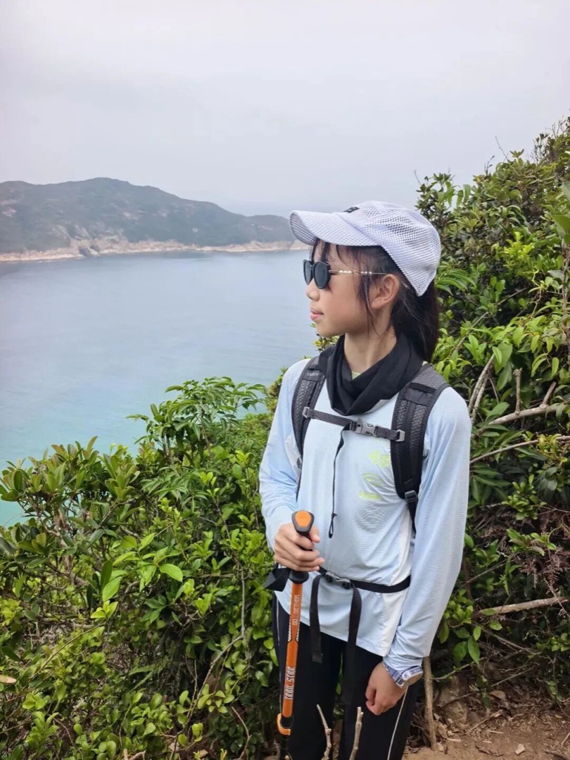 香港西湾山山脊上，背登山包持登山杖眺望大浪湾海岸的孩子